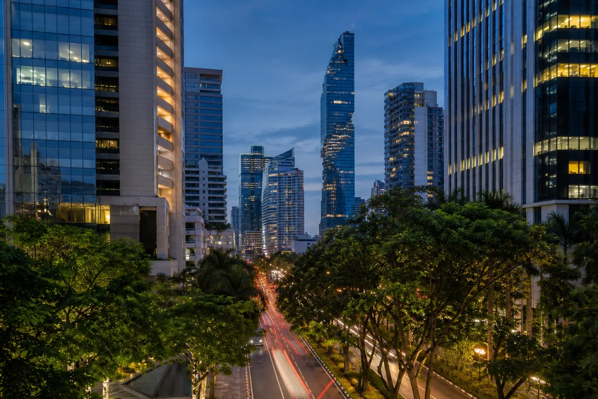 Silom and Sathorn towers rising beyond mature trees at blue hour